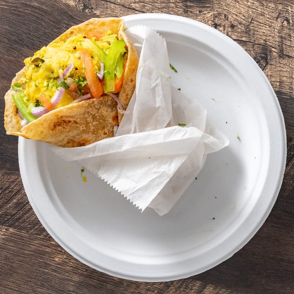 A colorful wrap filled with yellow scrambled eggs, red tomatoes, green peppers, and red onions.
