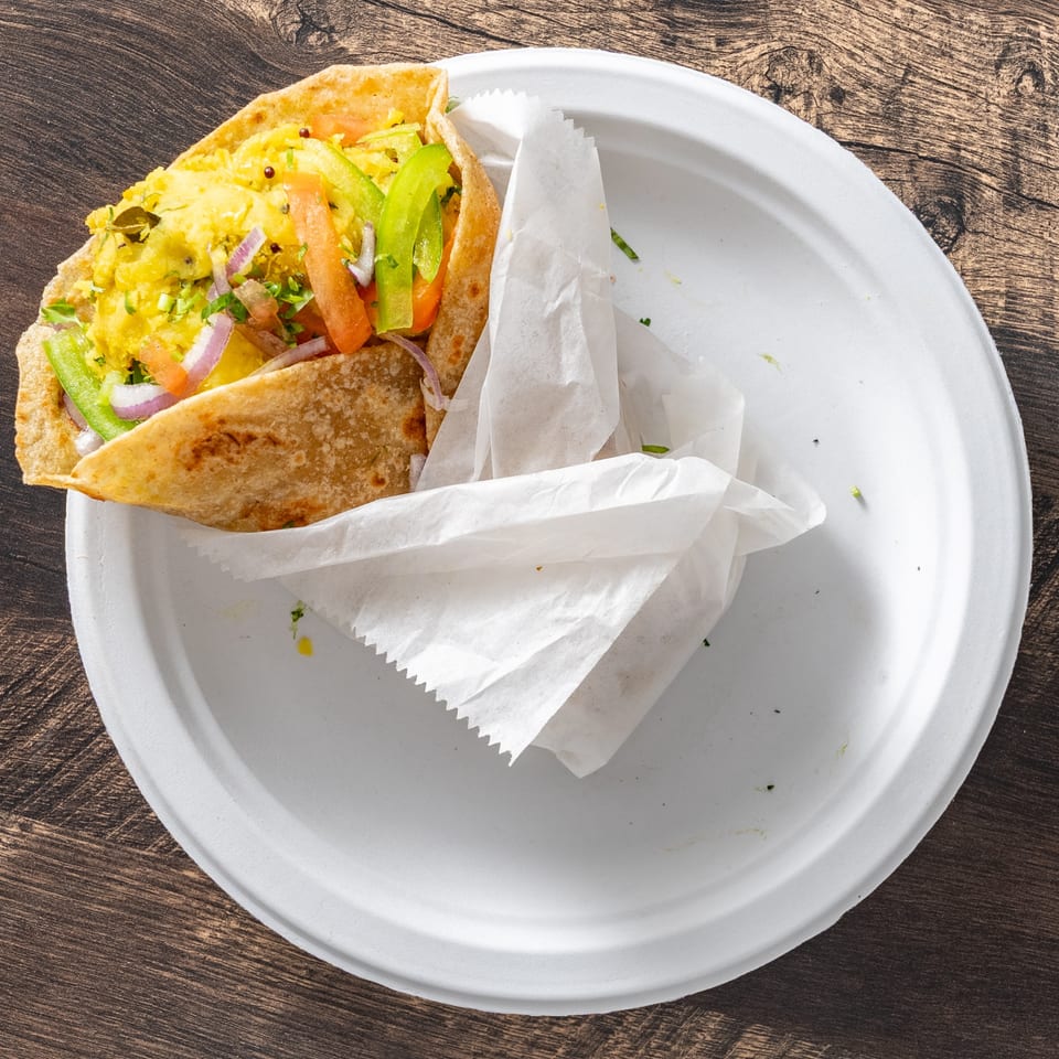 A colorful wrap filled with yellow scrambled eggs, red tomatoes, green peppers, and red onions.