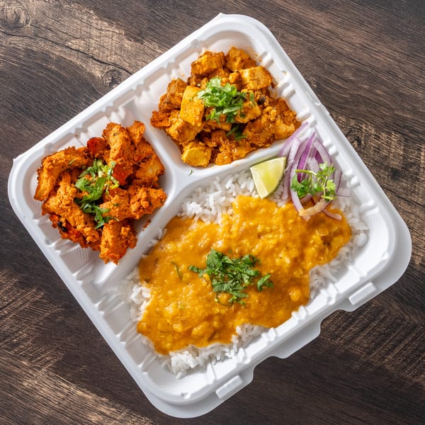 Indian takeout meal with chicken tikka, paneer, rice, dal, lime, and red onion in a white container.