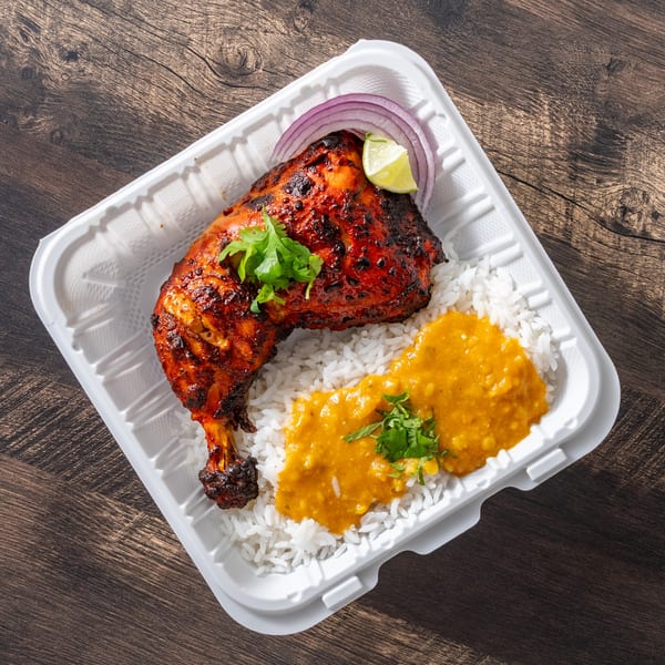 Tandoori chicken leg with rice, yellow lentil curry, red onion, and lime in a takeout container.