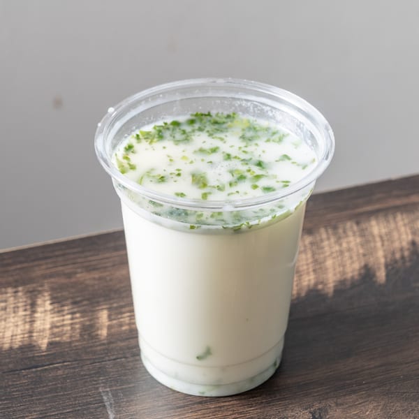 A clear plastic cup filled with a white drink topped with green herbs on a wooden table.