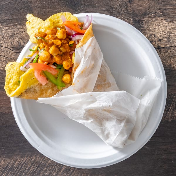 A chickpea wrap with vegetables and sauce, partially unwrapped on a white plate.