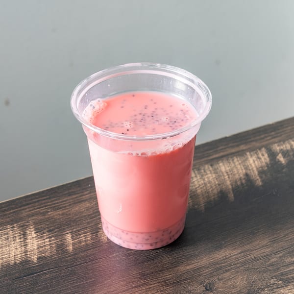 Pink drink with black seeds and foam in a clear plastic cup on a wooden table.