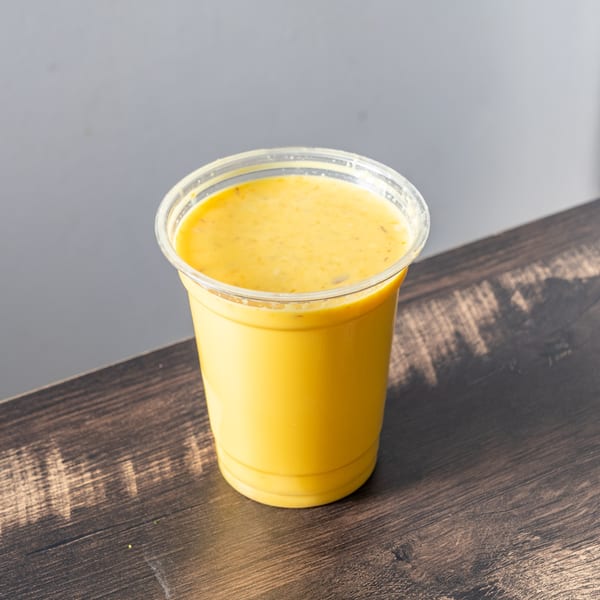 A yellow smoothie in a clear plastic cup sits on a dark wooden table.